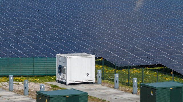 Aerial view of solar panels and a white power container on a solar farm with green electrical boxes and dandelions Warmenhuizen, North Holland, Netherlands.