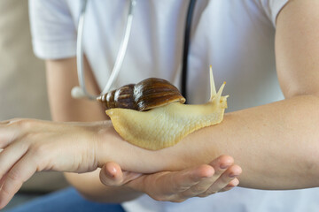 a large achatina snail moves slowly across a human arm during a professional skincare procedure held by a specialist in a white uniform with a stethoscope in a bright clinical environment © Lana Pietukhova