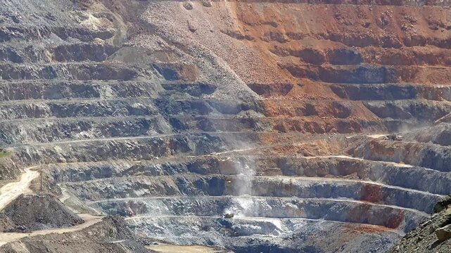 Terraced open pit mine site with scraped mountain slopes and a vast excavation crater in operation. Industrial, operations, production, machinery show industrial process heavy operations.