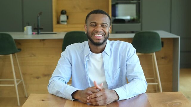 Confident african american businessman talking and gesturing during an online meeting, smiling and looking directly at the camera while sitting at his modern kitchen table for a video chat