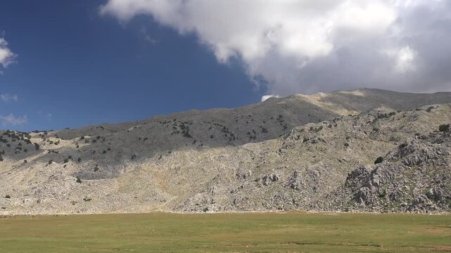 Timelapse of treeless rocky Taurus Mountains edge above flat plain with green meadows in Turkey. Barren terrain, summer weather, and arid landscape support rural farming themes for stock search value.