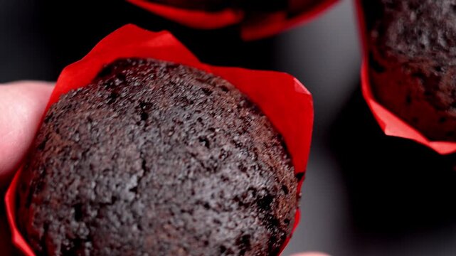 Hand taking a chocolate cupcake with dark porous texture in a red paper baking cup from a black platter