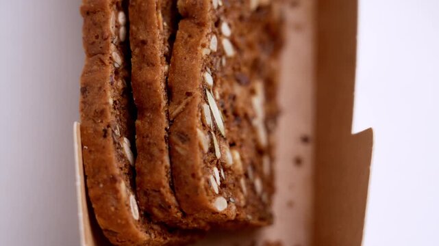 Close-up of a human hand picking a healthy wholegrain rye cracker with sunflower and flax seeds from a brown paper pack. Concept of artisanal bakery products