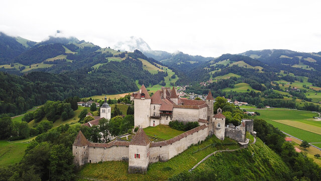 Aerial view of Chateau de Gruyeres with its stone walls and towers overlooking the lush green alpine landscape and rolling hills Gruyeres, Fribourg, Switzerland.