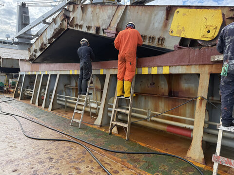 ship crew painting coaming of ship cargo holds. hatch covers opened by pyramid. team work. seafarers life.