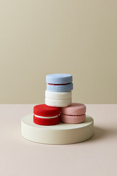 Macaron-like sponge stacks on cylindrical stand against a clean two-tone beige background.