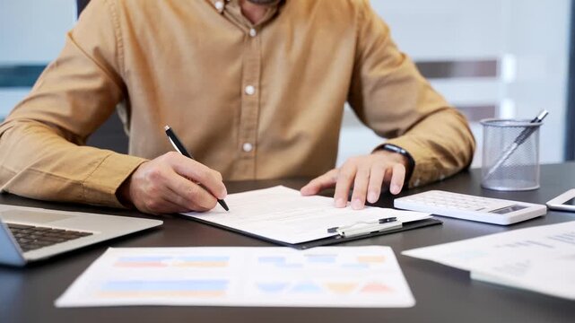 Close up of businessman hands calculating on calculator and writing notes at desk in office, checking numbers and recording results. Accounting tasks, financial control and precise paperwork workflow.