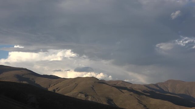 Cloud movement over treeless arid Zagros mountains near Shiraz Iran creates desert landscape. Slow clouds drift above barren hills showing dry climate, empty terrain, and atmospheric motion.
