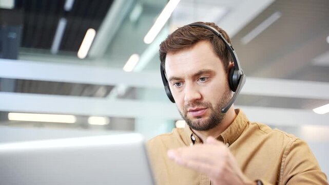 Close up of businessman in headset conducting online training on laptop at desk in office, speaking during session. Coaching, mentoring, knowledge transfer in professional corporate learning workflow.
