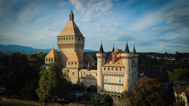 Aerial view of the historic Vufflens-le-Chateau castle featuring its massive central keep and pointed turrets under a soft blue sky Vufflens-le-Chateau, Vaud, Switzerland.