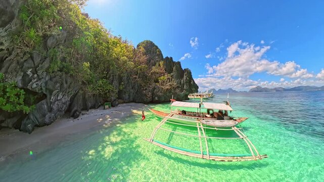 Traditional bangka boats rest in turquoise shallows off Entalula Beach,framed by white sand, towering limestone cliffs and lush tropical greenery under blue sky in El Nido, Philippines, Palawan island