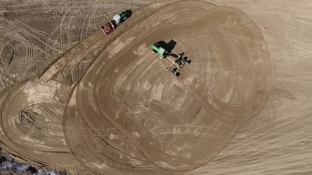 Aerial view shows tractors and field machines leveling treeless brown farmland from above. Agricultural vehicles reshape the soil across broad rural parcels in a working landscape.