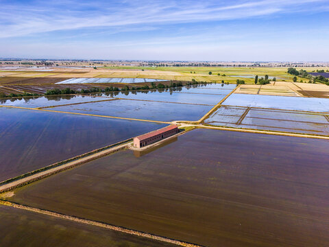 Aerial view of Tenuta Colombara surrounded by flooded rice fields and rural landscape under a blue sky in Livorno Ferraris, Piemonte, Italy.
