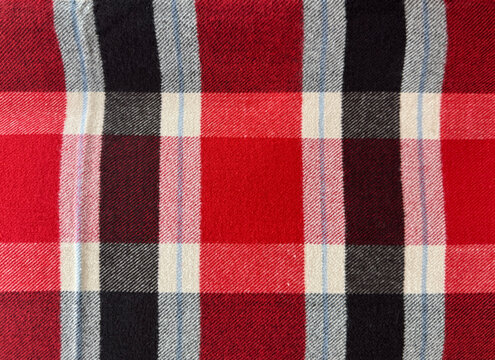 Close up of red flannel fabric with tartan pattern. In red, black, and white color. Flannel or tartan style is very common in scarf, shirts, and fashion industry. Seamless background texture.