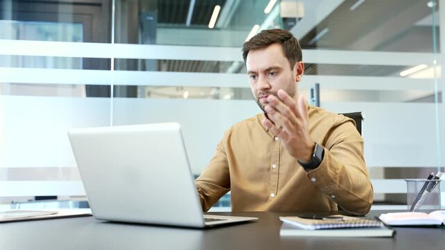 Frustrated businessman facing technical problem on laptop while sitting at desk in office, reacting to error with stress. Work difficulties, deadline pressure and problem solving in corporate workflow