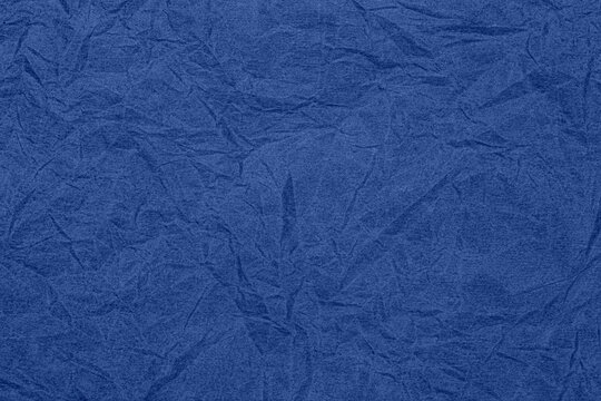 Crinkled blue paper texture shows subtle wave patterns and depth in light, suitable for backgrounds and designs