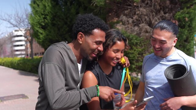 Multiethnic friends in sportswear laughing and taking a selfie with a smartphone after a training session in a park on a sunny day