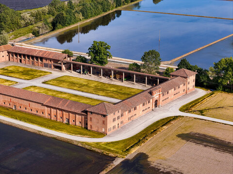 Aerial view of the historic Tenuta Colombara farm complex with its red brick buildings and flooded rice paddies in Livorno Ferraris, Piemonte, Italy.