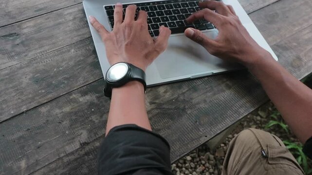 Top view of hands typing on a laptop placed on a rustic wooden desk