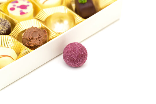 Assorted chocolates and a purple candy outside a box on a white background in a sweet display during daytime