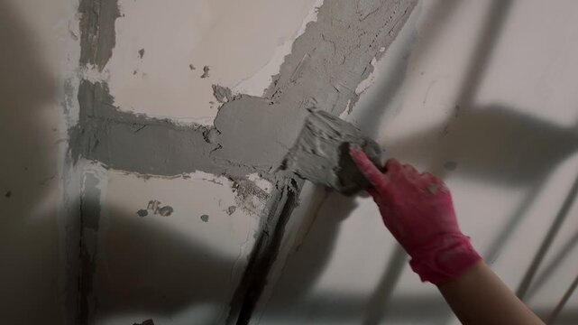 Repairing damaged wall corner with plaster and gloved hand