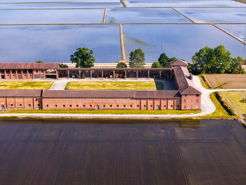 Aerial view of Tenuta Colombara historic farmstead with brick buildings and flooded rice fields in Livorno Ferraris, Piemonte, Italy.