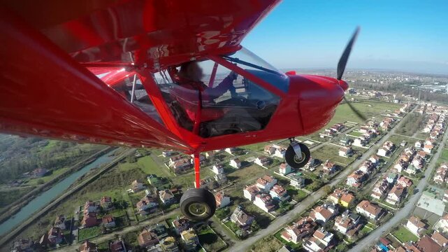 Red single seat propeller airplane approaches runway during controlled landing at airport. Small aircraft descends smoothly showing pilot cockpit view city below and spinning.