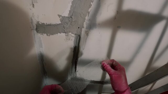 Hand in glove applying plaster on damaged wall surface