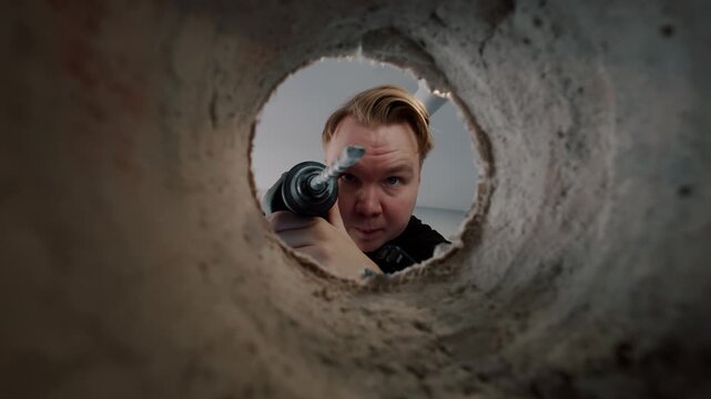 View through drilled hole at man using power drill
