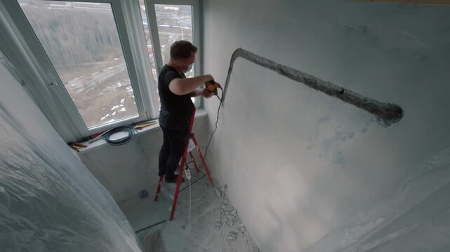 Man drilling wall near window during renovation