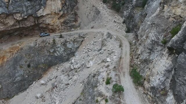 Aerial view of offroad suv driving narrow rocky mountain pass valley Himalayas dangerous remote. Rugged track winds across high peaks showing extreme terrain and isolation beside vehicle.