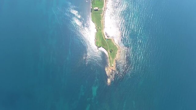 Panoramic aerial view of elongated promontory peninsula extending into blue sea at sunrise. Natural landform shows green narrow headland surrounded by calm waters and coastal textures.