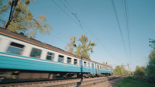 Blue Passenger Train Moving Fast Along Railway Track | Suburban Electric Train in Motion with Motion Blur | Ultra-Wide Side View on Sunny Spring Day