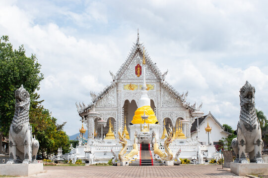 Beautiful white Thai temple architecture featuring a central white stupa wrapped in yellow cloth, flanked by ornate golden pagodas and two large guardian lion statues in the foregroundใ