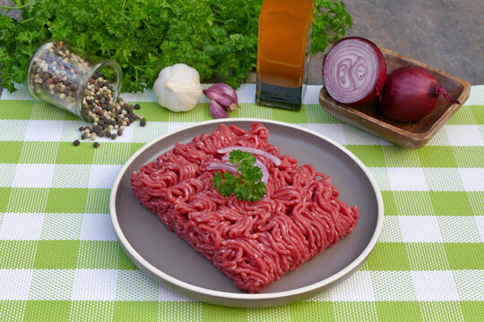 Fresh minced beef with onions, garlic and herbs on a green and white checkered tablecloth.