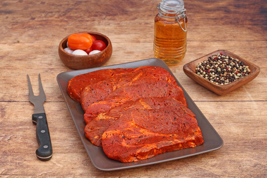 Marinated pork neck steaks with spices and a meat fork on a rustic wooden background.