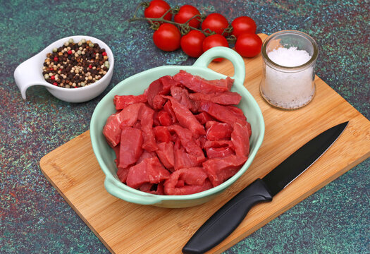 Strips of raw beef in a bowl with spices and tomatoes on a wooden board.