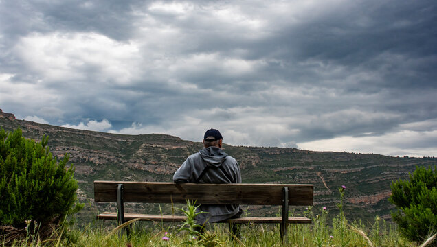 Hombre sentado en un banco contemplando un paisaje de monta&ntilde;a en invierno.