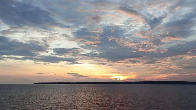 Dramatic tropical sunset sky over the Maluku sea with island silhouette and calm ocean waves, Indonesia