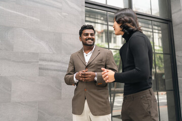 Smiling man and woman talking near office window in urban building
