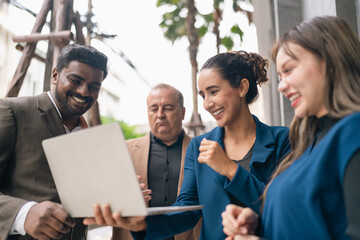Fototapeta premium Smiling business team reviewing laptop outdoors in modern office setting