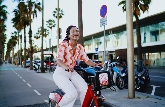 Calm young woman cycling red bike with peaceful smile, representing digital mobility, independent lifestyle and balance of modern femininity with urban freedom.