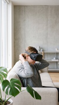 Young woman putting on a virtual reality headset while sitting on a sofa in a modern living room