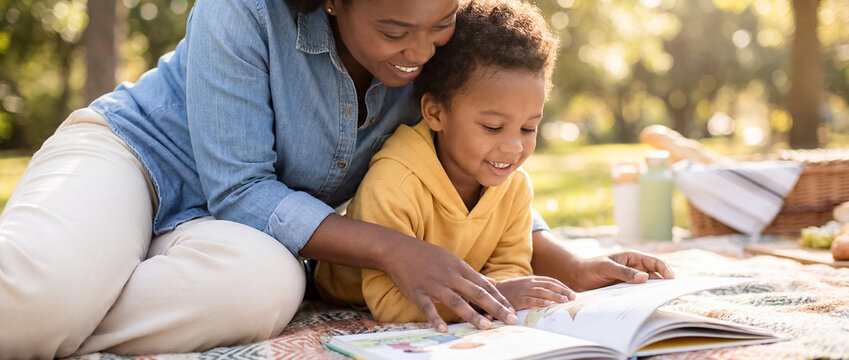 african american mother son reading book park picnic blanket family outdoor bonding learning close up of black mom and little boy enjoying story together lying on rug in sunny green summer garden
