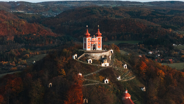 Aerial view of the Kalvaria Banska Stiavnica baroque church on a hill surrounded by vibrant autumn forests during golden hour in Banska Stiavnica, Banskobystricky kraj, Slovakia.