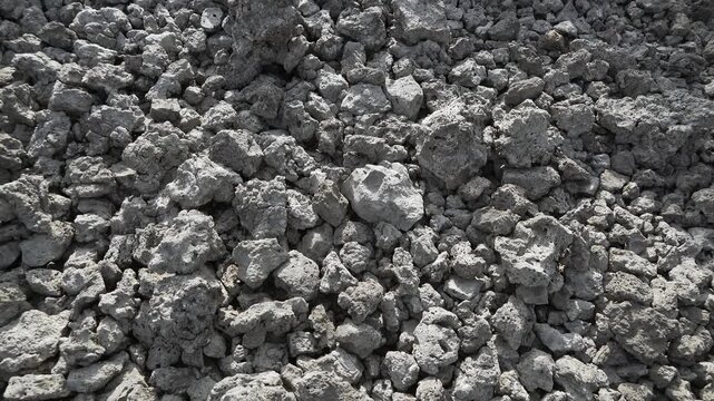Basalt lava plain with porous volcanic rocks and sparse vegetation forms a harsh landscape. Dark igneous stone, cracked ground, weathered magma textures reveal raw geologic terrain.