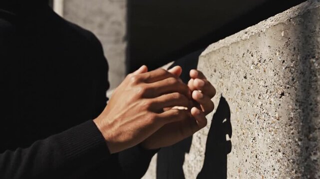 Man's hand touching rough concrete wall with shadow play