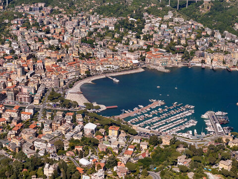 Aerial view of the city of Rapallo featuring the historic castle on the sea, the harbor, colorful buildings, a sandy beach, and numerous yachts in Rapallo, Liguria, Italy.