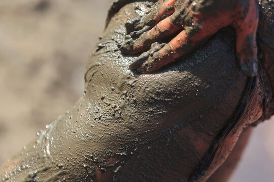 Close-up of hand resting on glistening mud-covered thigh for natural healing and detox skincare