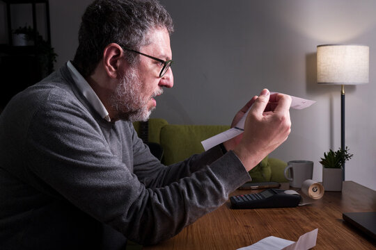 Adult man worried about bills and expenses while checking receipt at home